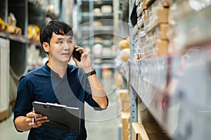 Man worker talking on a mobile phone and holding clipboard to checking inventory in the warehouse store