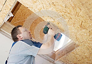 Man worker twists the into the ceiling with a screwdriver