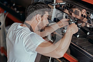 Man worker in uniform checking coffee machine in own workshop