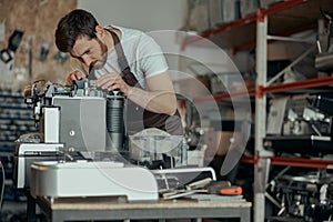 Man worker in uniform checking coffee machine in own workshop