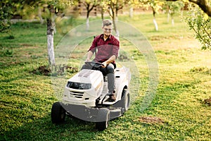 Man worker using ride on lawnmower, male riding lawn tractor and relaxing during sunset golden hour