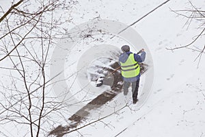 Man, worker in vest shoveling snow after snowfall on road, street