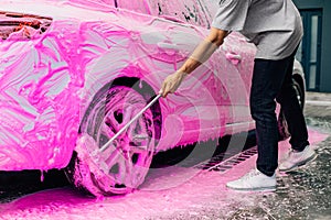 Man worker washes alloy rims of a car at a car wash, a man washes car rims with foam and a brush