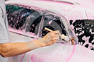 Man worker washes alloy rims of a car at a car wash, a man washes car rims with foam and a brush