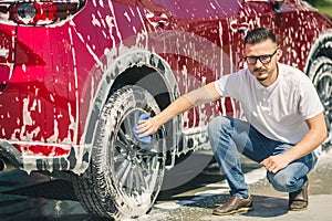 Man worker washing car`s alloy wheels on a car wash. Car wash with soap.