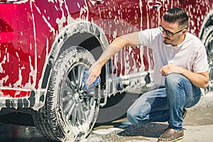 Man worker washing car`s alloy wheels on a car wash. Car wash with soap.