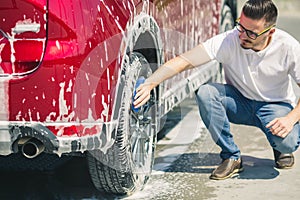 Man worker washing car`s alloy wheels on a car wash. Car wash with soap.