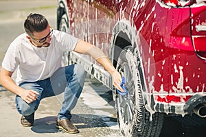 Man worker washing car`s alloy wheels on a car wash. Car wash with soap.