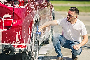 Man worker washing car`s alloy wheels on a car wash. Car wash with soap.