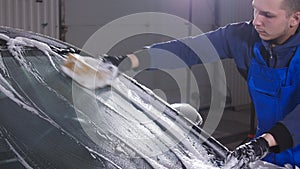 Man worker washing car with sponge on a car wash station