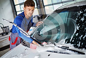 Man worker washing windshield with sponge on a car wash