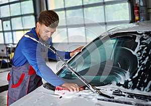 Man worker washing windshield with sponge on a car wash