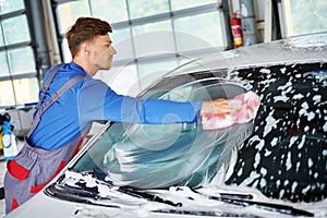 Man worker washing windshield with sponge on a car wash