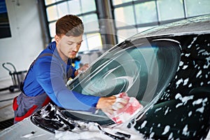 Man worker washing windshield with sponge on a car wash