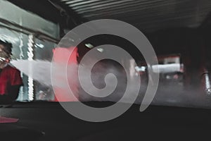 Man worker washing windshield with water on a car wash