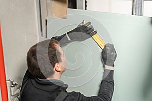 A man working Builder makes a marking on the drywall for electrical wiring. Metal drywall construction in a house during
