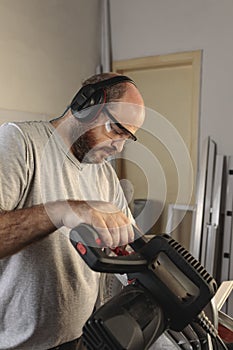 Man working in carpentry, operating an electric cutting machine. He wears protective goggles and ear protection. Concept of safe