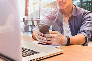 Man working on cell phone with laptop on wooden table