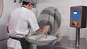 A man working at cheese production factory - adding a thickener into a vat with a cheese base