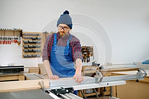Man working on circular saw and engaged in making wooden blank at workshop
