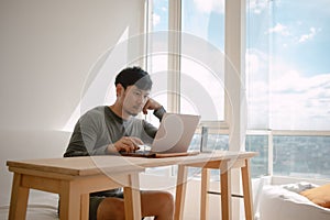 Man working with computer in apartment with city view at the windows in morning light.