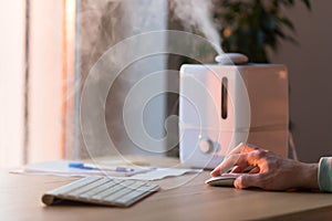 Man working on computer, using pc mouse near the aroma oil diffuser on the table, steam from humidifier, selective focus