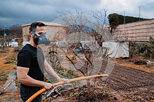 Man working in the fiel and watering whit antibacterial mask. photo