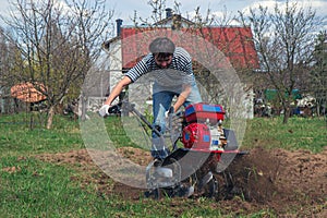 Man working in the garden with garden tiller. tractor cultivating and loosens soil field