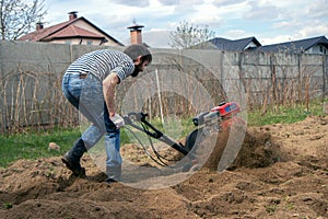 Man working in the garden with garden tiller. tractor cultivating and loosens soil field photo