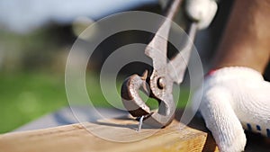 Man in working gloves pulls out the hammered nail from wood by rusty nail puller outdoors, backyard handmade, DIY stuff