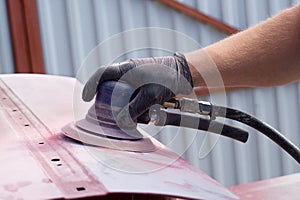 A man working with grinding tool. Sanding of car elements. Hands in black gloves hold a power tool.