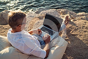 Man working on his laptop lying on deck chair on the beach during sunset