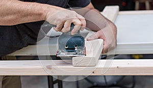 A man working on a home improvement project sanding wood with an electrical sander.
