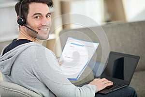 man working from home wearing headset and holding papers