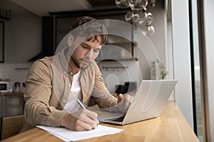 Man working from home writing up data from laptop screen