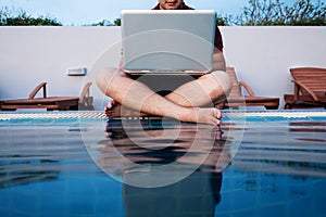 A man working on laptop computer, sitting at poolside, selective focus