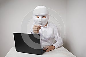 A man working at a laptop, covers his face with a mask, the concept of anonymity on the Internet