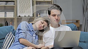 Man Working On Laptop while His Gril Sleeping with Head on His Shoulder