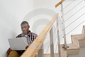 Man working on laptop while sitting on stairs in a comfortable home