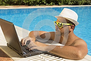 Man working on laptop at the swimming pool edge