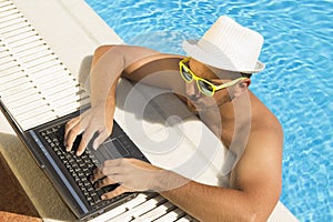 Man working on laptop at the swimming pool edge. Top down viewpoint