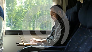 Man working on laptop tablet computer in train.