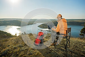 Man working on laptop on top mountains and relaxes near river at sunset.