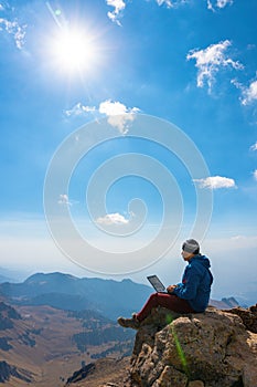 Man working on notebook sitting on cliff on top of the mountains photo