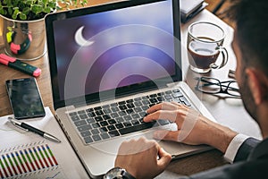 Man working in the office. Crescent moon on the computer screen,