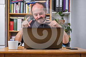 Man working online from home on computer laptop behind vintage desk, with earphones