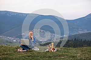 Man working outdoors with laptop sitting in mountains. Concept of remote work or freelancer lifestyle. Cellular network broadband