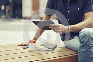 Man working outside in park using modern tablet, notebook, mobile phone. Wooden bench.