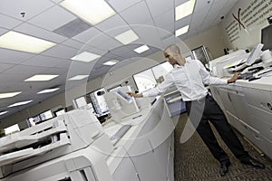 Man working in printing press between two cash register machine