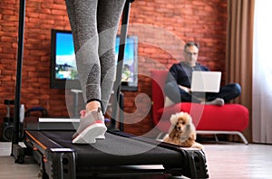 The man is working remotely. Woman exercising on a treadmill at home. Healthy lifestyle.